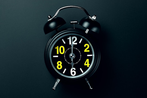 Un elegante reloj despertador negro con números amarillos y blancos sobre un fondo oscuro En blanco para el diseñador