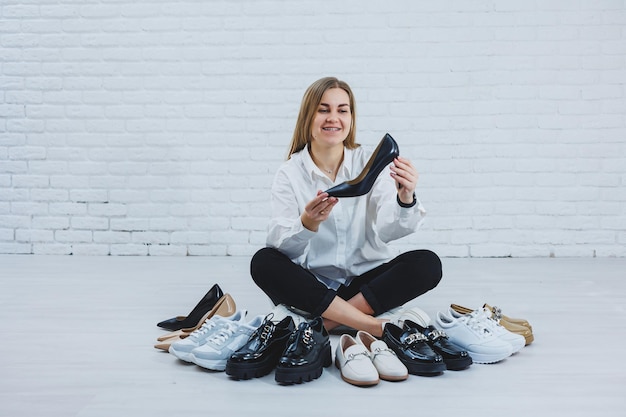 Elegante rubia eligiendo zapatos mientras está sentada en el suelo Vista lateral de muchos zapatos de mujer en el suelo una selección de zapatos con estilo