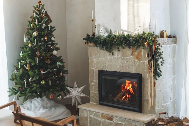 Elegante sala de estar navideña con árbol de Navidad decorado moderno con adornos antiguos y decoración escandinava en la chimenea con campanas y cinta Nochebuena atmosférica en una granja