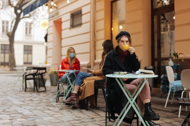 Elegante señorita sentada sola en la terraza de un café abierto y bebiendo café recién hecho.
