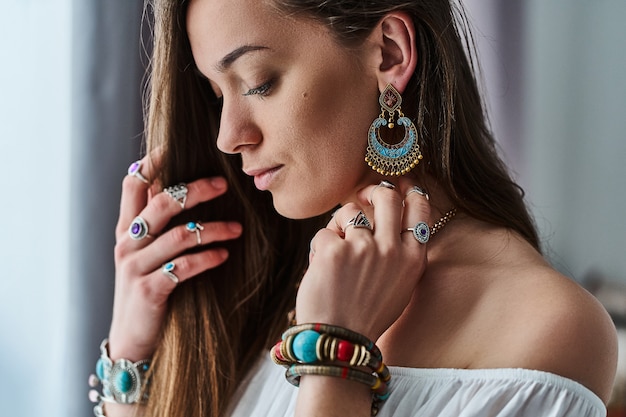 Elegante y sensual mujer boho chic en blusa blanca que usa grandes aretes, pulseras y anillos de plata. Traje bohemio gitano hippie indio de moda con detalles de bisutería