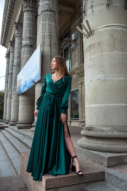 Elegante sexy Frau im langen grünen Kleid, das nahe Stadttheatersäule aufwirft