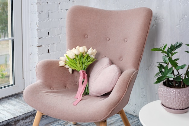 Elegante sillón rosa con almohada en forma de corazón y ramo de tulipanes en un interior minimalista y brillante.