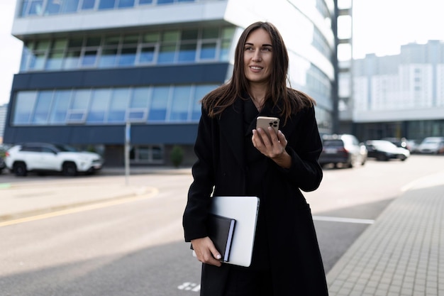 Elegante solide kaukasische Geschäftsfrau mit Laptop und Handy draußen