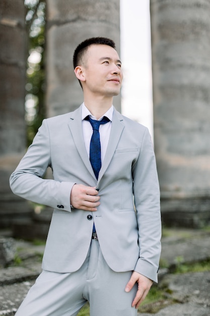 Elegante sonriente guapo novio asiático en traje gris posando