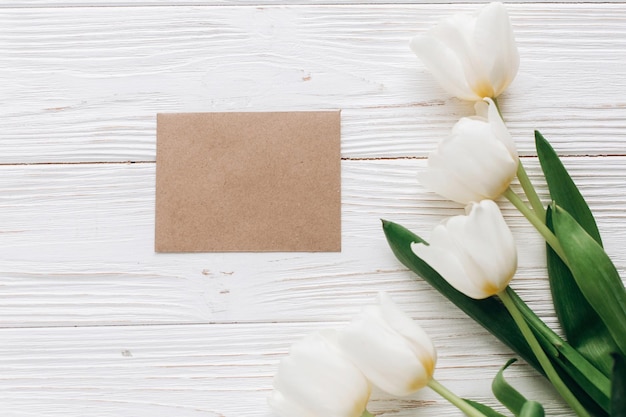 Elegante tarjeta de felicitación artesanal y tulipanes sobre fondo rústico de madera blanca plana con flores y papel en blanco de regalo con espacio para texto tarjeta de felicitación de concepto de feliz día de la mujer de la madre