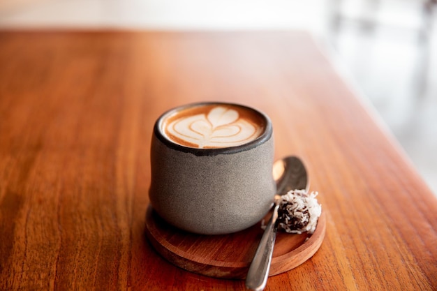 Elegante taza gris de capuchino caliente con arte latte sobre fondo de mesa de madera Una taza para la rutina matutina