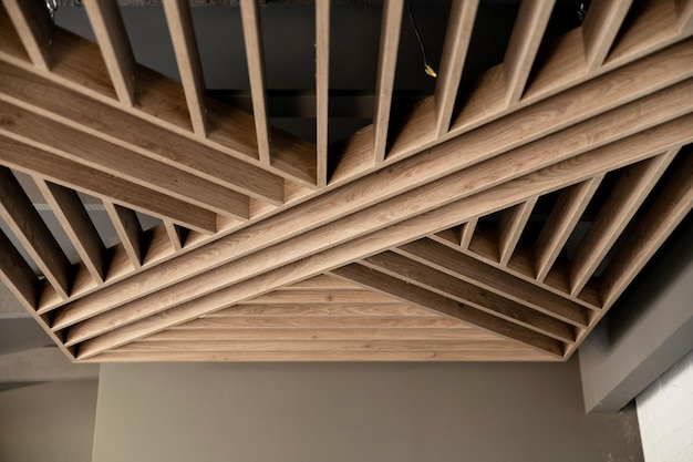 Elegante techo falso de madera en el techo moderno de la casa, la plataforma de madera está suspendida de vigas de madera grises, reparación ecológica del techo