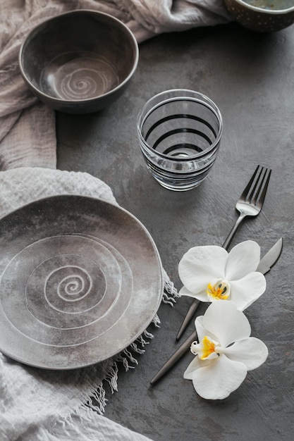 Elegante Tischdekoration mit gestrickter grauer Serviette, Besteck, Keramiktellern, Gläsern und weißen Orchideenblüten