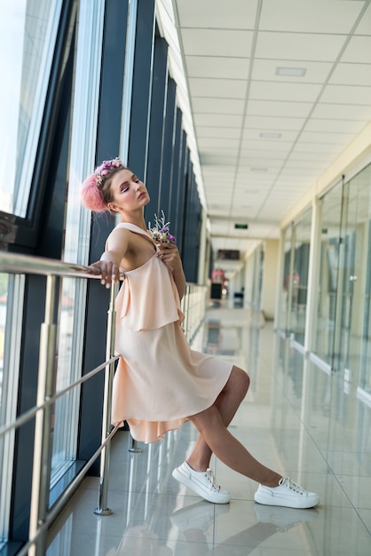 Elegante und junge Frau im rosa Kleid, die im langen Korridor aufwirft