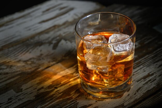 Elegante vaso de whisky en una rústica mesa de madera iluminada por una suave iluminación