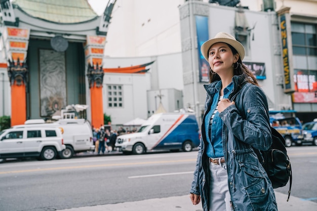 Foto elegante viajante feminina relaxante em frente ao teatro chinês com um sorriso confiante no rosto. mochileiro feliz tendo férias nos eua. destino de primavera de la.