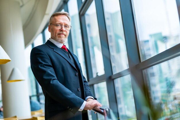 Eleganter älterer Mann in dunklem Anzug und roter Krawatte blickt von unten auf das Panoramafenster