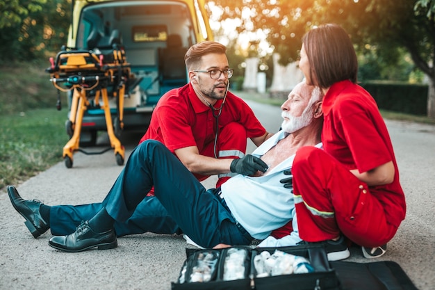 Foto eleganter älterer mann mit herzinfarktsymptomen, der auf der straße sitzt und versucht, ihm zu helfen. fahrerassistenzdienst.