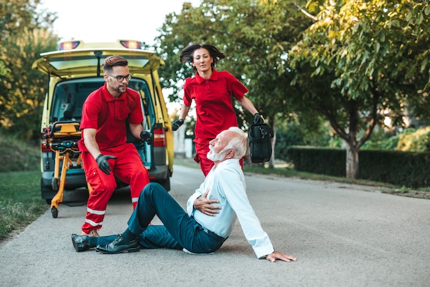 Foto eleganter älterer mann mit herzinfarktsymptomen, der auf der straße sitzt und versucht, ihm zu helfen.