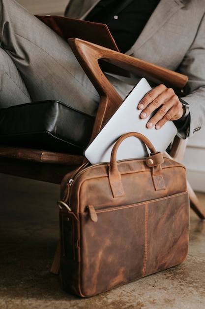 Foto eleganter geschäftsmann, der seinen laptop in seine braune ledertasche steckt