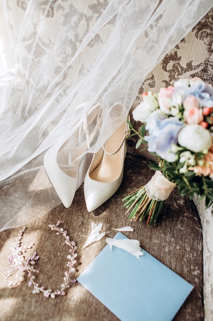 Eleganter Hochzeitsstrauß mit Band, Hochzeitseinladungen, Verlobungsringen und Schuhen für die Braut auf einem Stuhl.