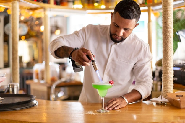 Eleganter junger lateinamerikanischer Kellner bereitet in einem modernen Restaurant sorgfältig ein alkoholisches Getränk zu. Platz für Text. Selektiver Fokus.