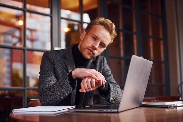 Eleganter junger Mann in formeller Kleidung sitzt mit seinem Laptop im Café.