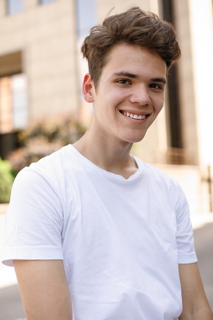Foto eleganter junger mann lächelt in einem modischen schwarzen hemd in einem weißen stylischen t-shirt in schwarzer hose mit trendiger frisur liegt in der nähe eines modernen geschäftszentrums. nahaufnahmeportrait