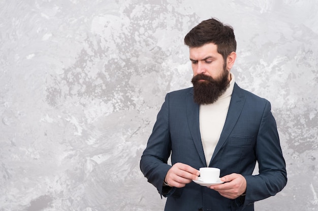 Eleganter Mann mit Bartgetränkkaffee. Brutaler bärtiger Hipster im Anzug. Männliches Modemodell. Reifer Geschäftsmann. Modernes Leben. Schneider oder Modedesigner. Aufwärmen mit frischem Kaffee. Mehr Kaffee.