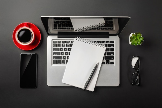 Eleganter schwarzer bürodesktop mit laptop, notizbuch, rotem tasse kaffee und handy. ansicht von oben.