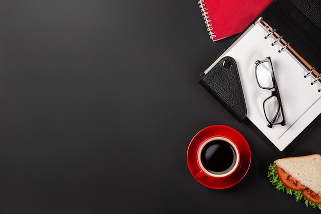 Eleganter schwarzer Bürodesktop mit Laptop, Tasse Kaffee und einem Sandwich zum Mittagessen. Ansicht von oben