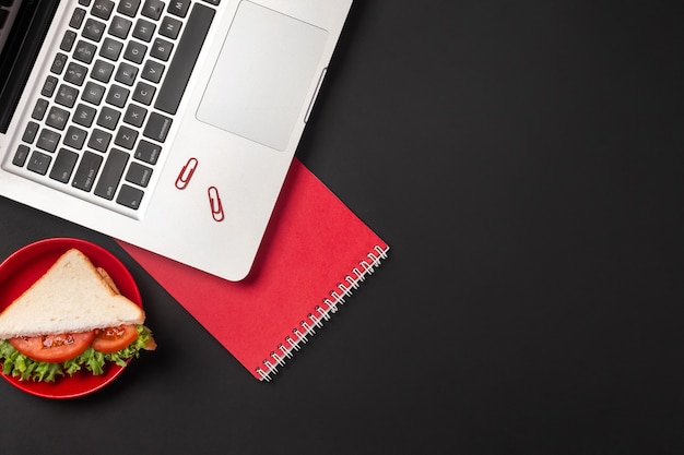 Eleganter schwarzer Bürodesktop mit Laptop und Sandwich zum Mittagessen. Draufsicht mit Kopienraum.