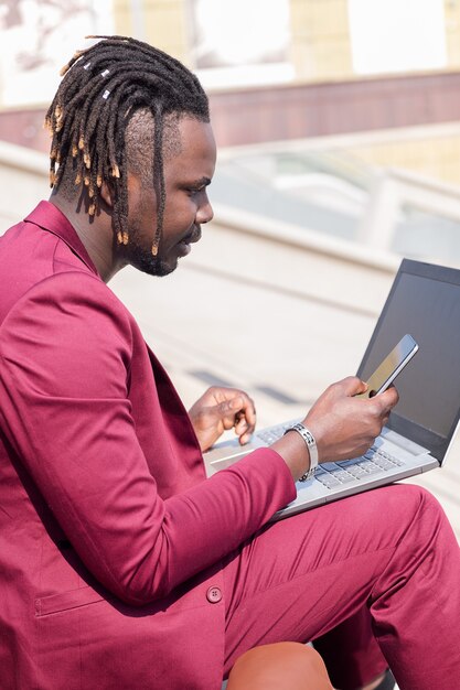 Eleganter schwarzer Mann, der mit Laptop und Telefon arbeitet