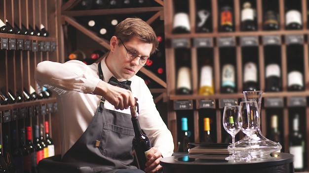 Eleganter Sommelier mit Fliege entkorkt eine Flasche Wein in einer Weinboutique