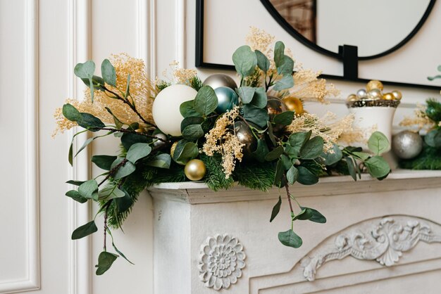 Eleganter Weihnachtskranz mit goldenen und silbernen Kugeln auf einem Kamin. Helles Interieur in Weißtönen