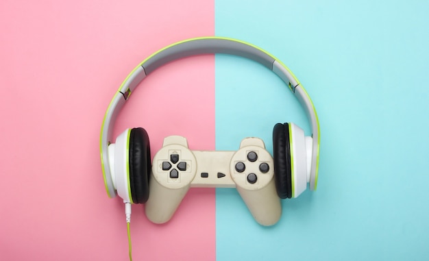 Elegantes auriculares estéreo con cable con gamepad en superficie rosa y azul