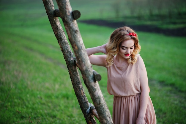 Elegantes blondes Mädchen Yong am Rosenkleid auf dem hölzernen Treppenhaus des Gartenhintergrundes.