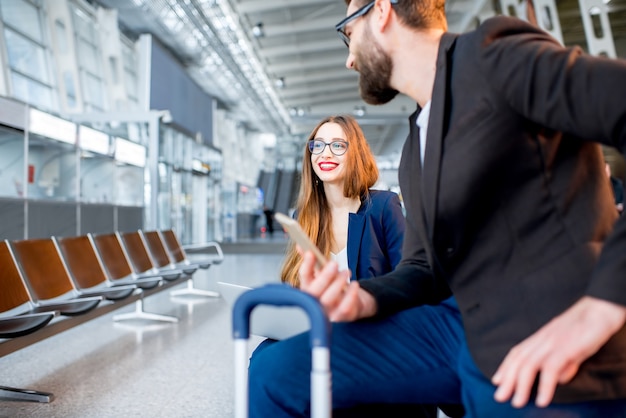 Elegantes Geschäftspaar, das mit Laptop und Gepäck in der Wartehalle des Flughafens sitzt. Ein geschäftliches Gespräch während der Fahrt am Flughafen führen