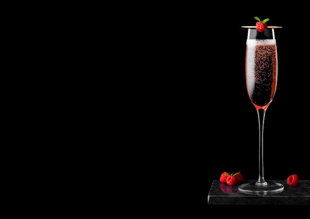 Elegantes Glas rosa Rosenchampagner mit Himbeere am Stiel mit frischen Beeren und Minzblatt auf schwarzem Marmorbrett auf schwarzem Hintergrund