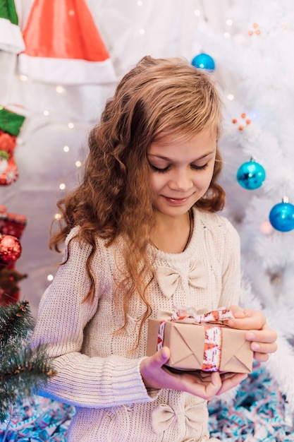 Elegantes Mädchen des neuen Jahres nahe einer grünen verzierten Fichte, die Geschenke hält