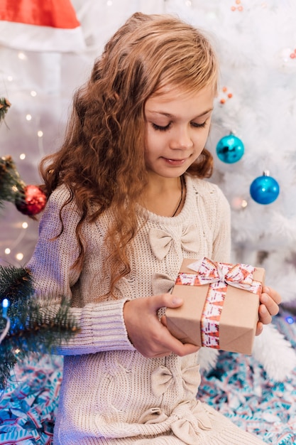 Elegantes Mädchen des neuen Jahres nahe einer grünen verzierten Fichte, die Geschenke hält