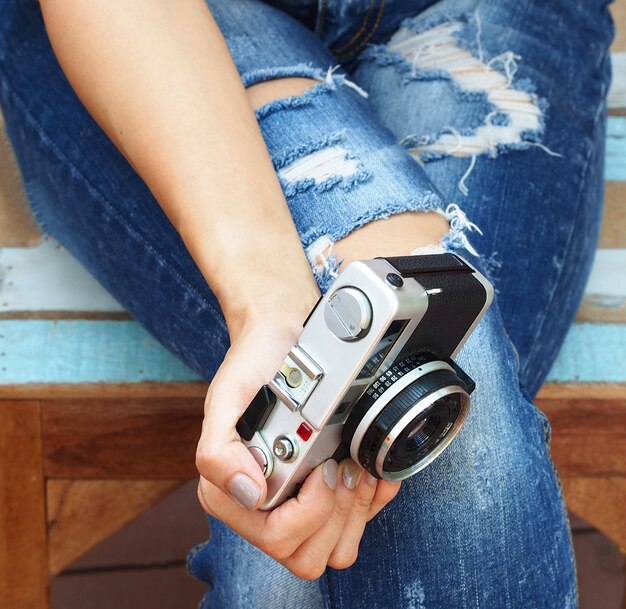 Elegantes mulheres sentadas em jeans rasgados com câmera velha