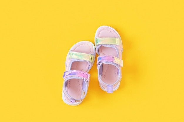 Elegantes sandalias holográficas para niños sobre fondo amarillo Zapatos de verano de moda brillante Vista superior plana