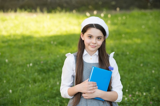 Elegantes Schulmädchen mit Buch im Park, anspruchsvolles Schulmädchenkonzept.