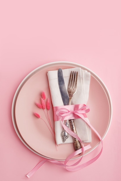 Elegantes stilvolles Gedeck. Messer und Gabel auf einer Serviette auf einer Platte auf einer rosa Oberfläche.