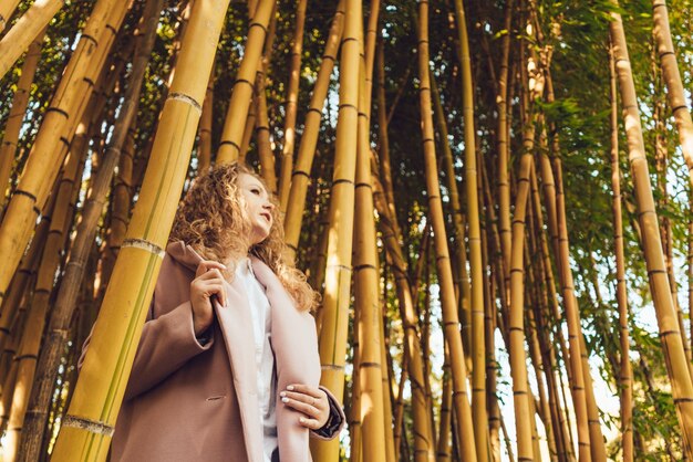 Elegantes, stilvolles Mädchen, das den Frühling genießt und sich im Park neben den Bambusbäumen entspannt