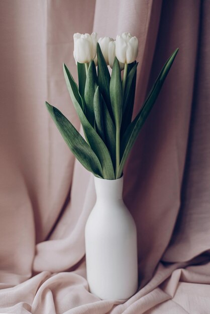 Elegantes tulipanes blancos en jarrón minimalista sobre fondo de tela beige en luz suave hola espacio de concepto de primavera para texto ternura momento atmosférico boda rústica