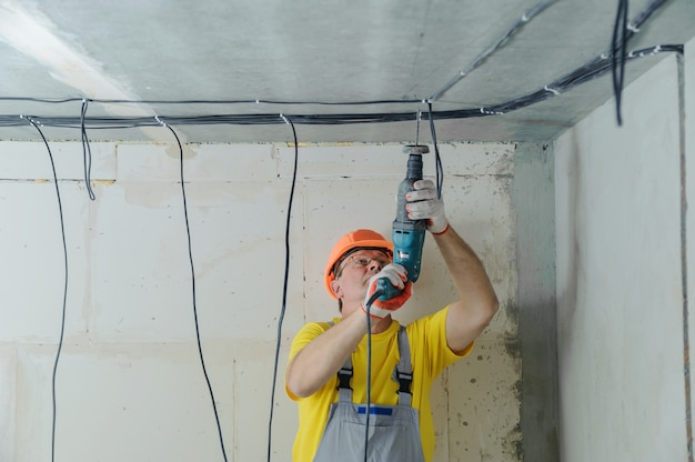 Elektriker bohrt eine Decke mit einem Perforator, um elektrische Kabel zu befestigen