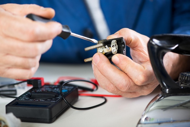 Elektriker, der alten Netzstecker vom Eisen überprüft und repariert. Nahansicht. Selektiver Fokus, Fokus auf Netzstecker.