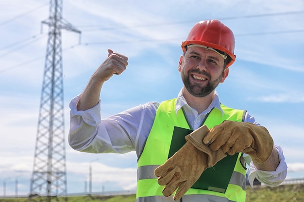 Elektriker, der in einem Helm mit Handschuhen arbeitet, steht auf einem Feld