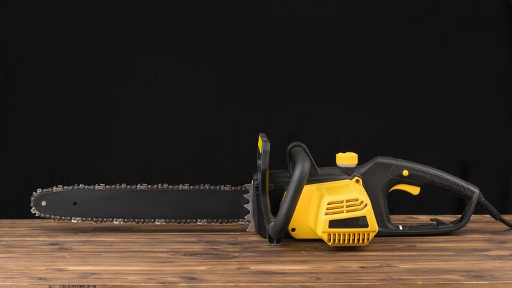 Elektrische Kettensäge auf einem Holztisch auf einem schwarzen Hintergrund. Elektrowerkzeug für die Holzverarbeitung.