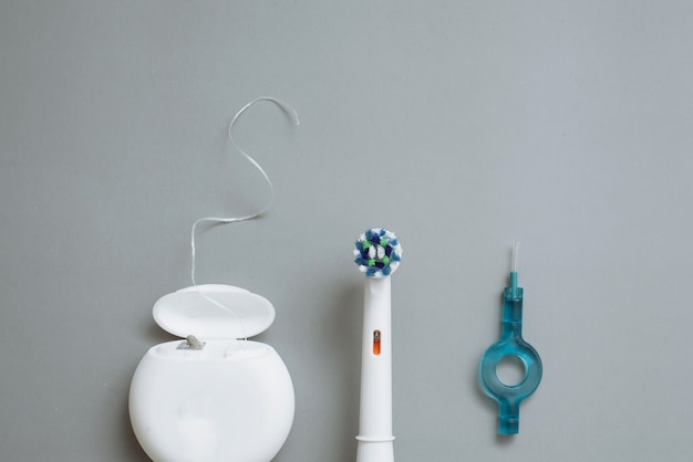 Elektrische Zahnbürste, Zahnseide und Interdentalbürsten auf grauem Hintergrund.