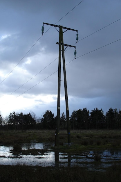 Foto elektrizitätsmast auf dem feld gegen bewölkten himmel