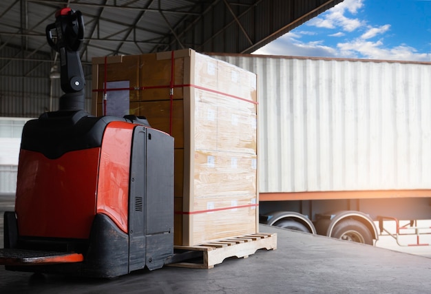 Elektro-Gabelstapler-Palettenheber mit Paketboxen laden mit Frachtcontainer-Anhänger-LKW geparkt im Dock-Lager